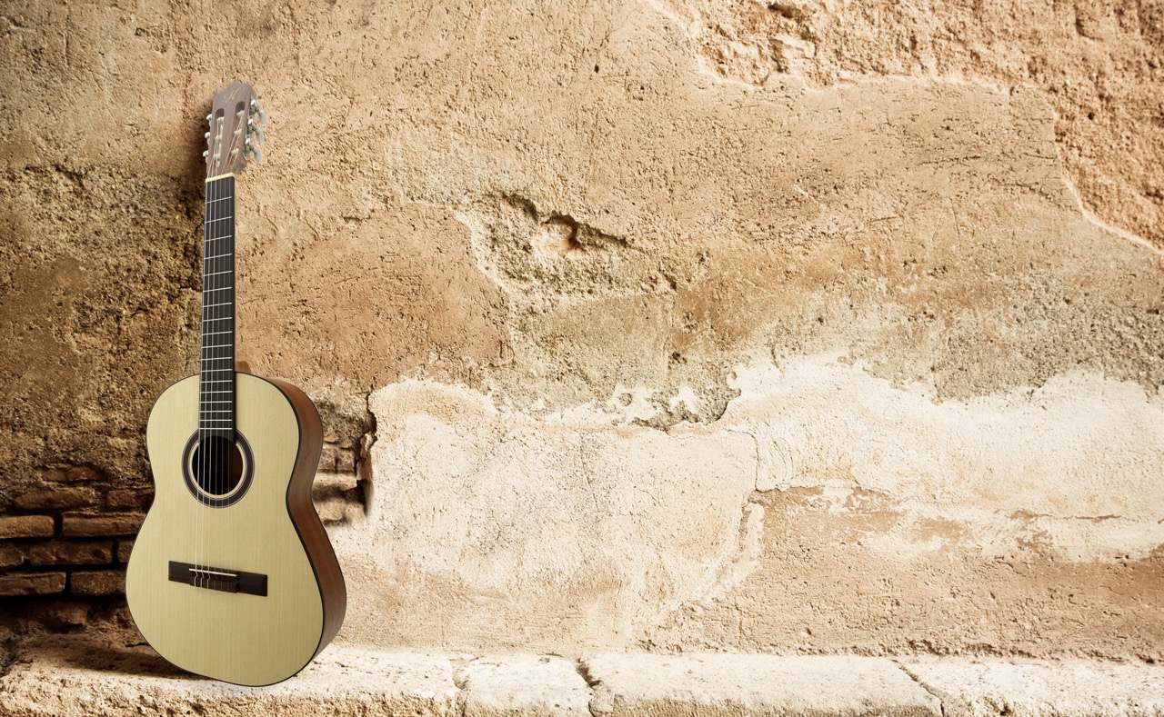 Light-colored acoustic guitar leaning against a weathered, textured plaster and stone wall.